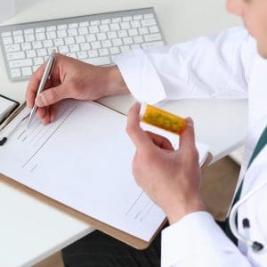 Male medicine doctor hand hold jar of pills and write prescription to patient at worktable. Panacea and life save, prescribing treatment, legal drug store concept. Empty form ready to be used